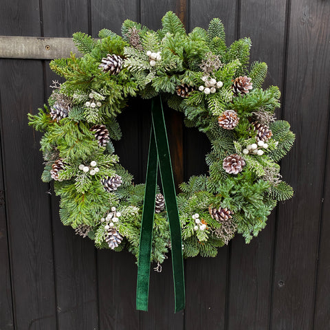 Christmas wreath with greenery, pinecones, and berries on a dark wooden background