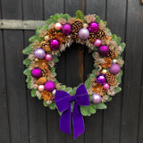 Decorative wreath with purple ornaments and a bow on a dark wooden background