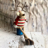 Toy reindeer wearing a striped sweater and red scarf against a wooden background