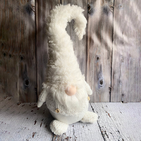 White plush gnome sitting on a wooden surface with a rustic wooden panel background