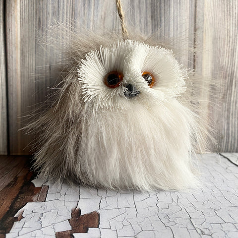 Plush owl toy with white face and brown eyes on a textured surface