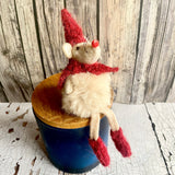 Small stuffed mouse with a red hat and scarf sitting in a blue pot against a wooden background