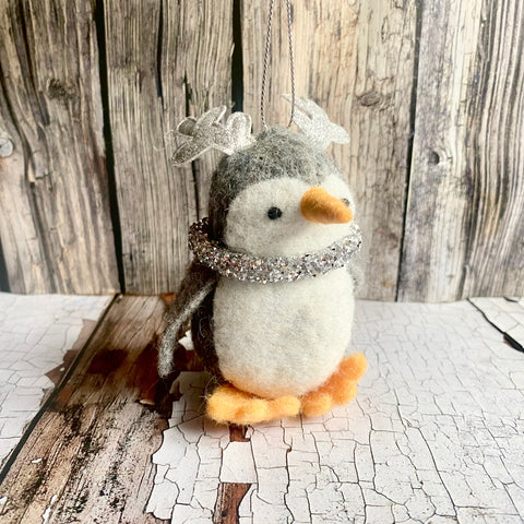Decorative penguin ornament with antlers and a silver collar on a rustic wooden background