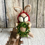 Stuffed animal resembling a rabbit holding a green wreath against a wooden background