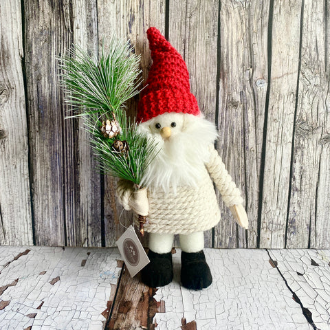 Decorative santa with a red hat and white beard holding a branch against a wooden background