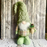 Green gnome figurine with plaid shirt and pine cone against a wooden background