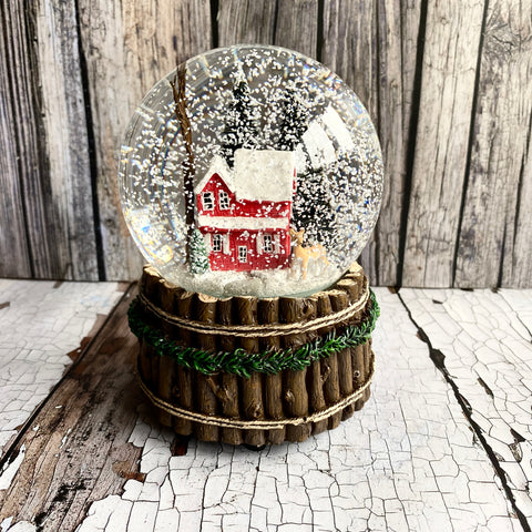 Snow globe with a red house inside, placed on a wooden base against a rustic wooden background.