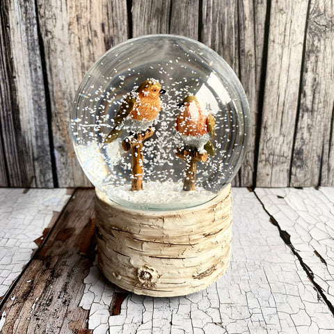 Snow globe with two birds on a wooden base against a wooden background