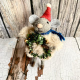 Felted mouse ornament with a red hat and green wreath on a wooden surface