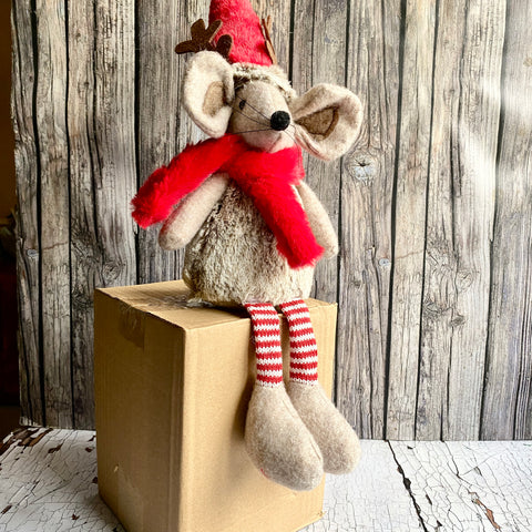 Stuffed mouse with a red scarf and hat on a wooden box against a rustic wooden wall.