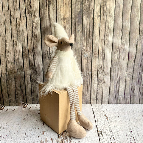Stuffed animal resembling a mouse with striped legs sitting on a cardboard box against a wooden background