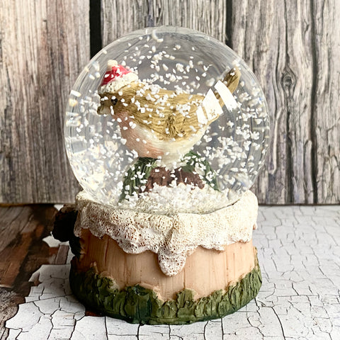 Snow globe with a robin inside on a textured log