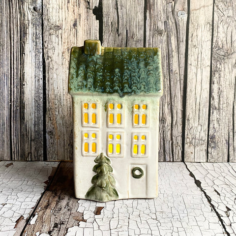 Ceramic house-shaped object with green roof and yellow windows on a wooden surface