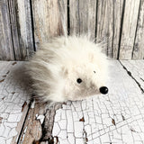 Plush toy hedgehog on a cracked white surface with wooden background
