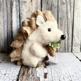 Stuffed hedgehog holding a pine cone on a wooden surface with a rustic background