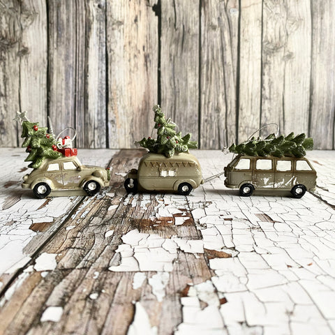 Three toy cars, campervan and caravan with Christmas trees on a rustic wooden surface